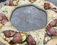 Step <p>Añadimos encima del tomate la mozarella a trozos, un poco de orégano, unas rodajas de calabacín y encima bacon o jamón york.</p><p>Cerramos los triángulos hacia fuera y espolvoreamos con un poco de queso rallado.</p> illustration